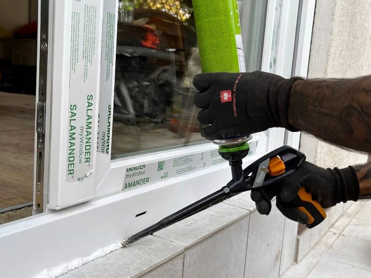 Monteur bringt Montageschaum an der Anschlussfuge eines Salamander-Fensterprofils auf